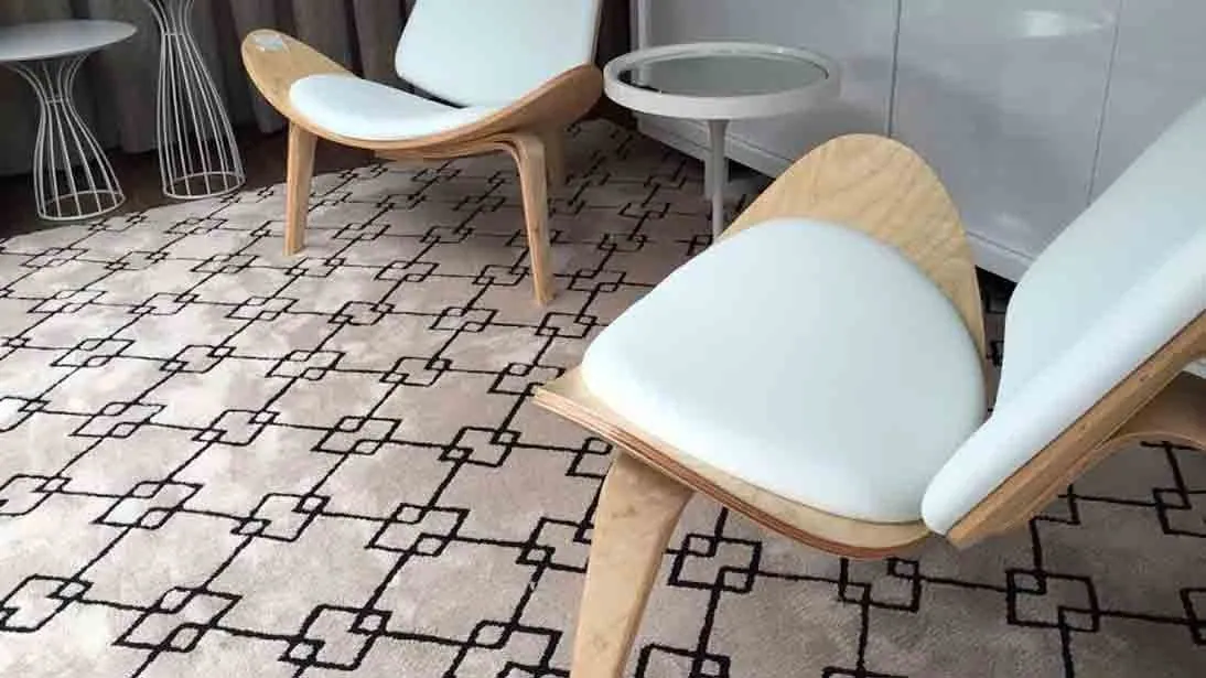 Tapete claro com linhas geométricas sob poltronas de madeira e estofamento branco
