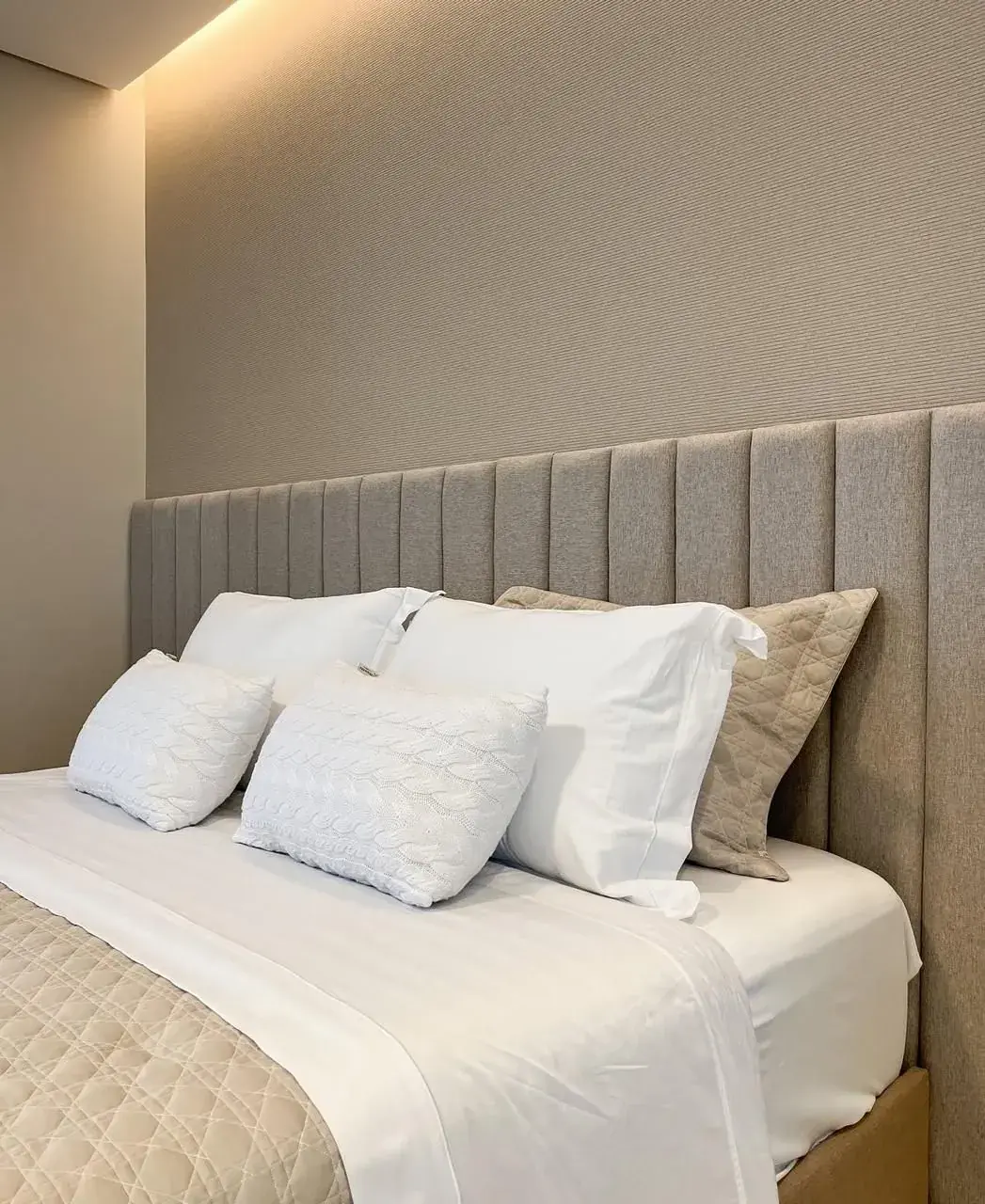 Cabeceira cinza com painéis verticais atrás de uma cama branca