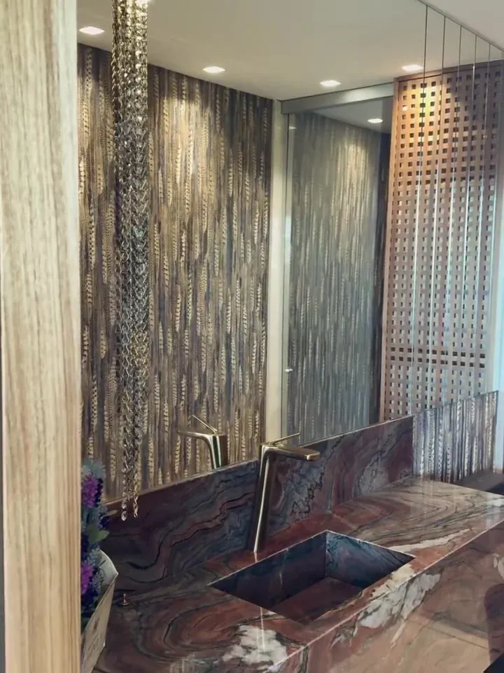 Lavabo com papel de parede de desenho vertical, bancada de veios marcantes, cuba retangular e metal em tom dourado