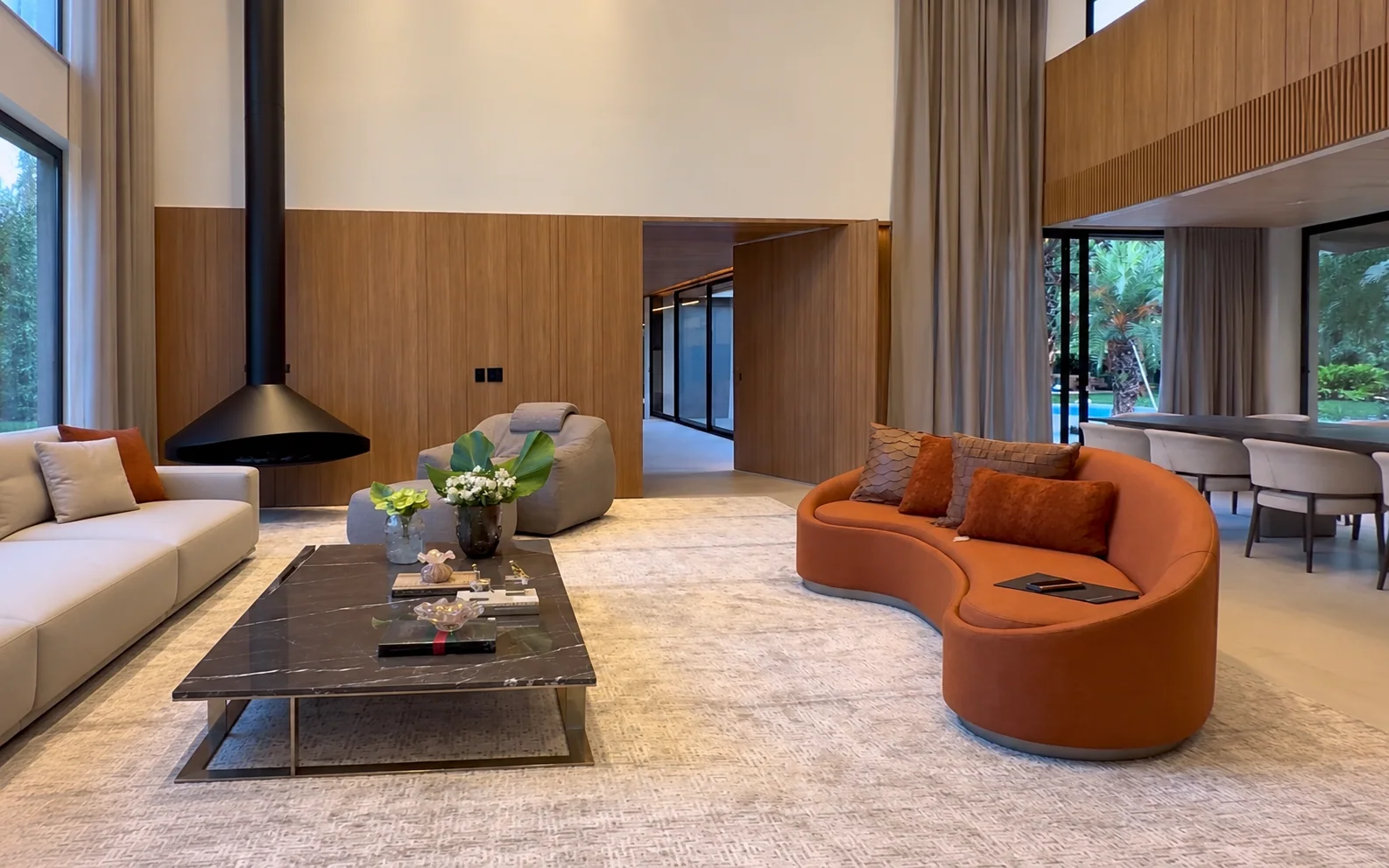 Sala com pé-direito duplo, cortinas e poltrona curva alaranjada — capa adaptada da imagem original