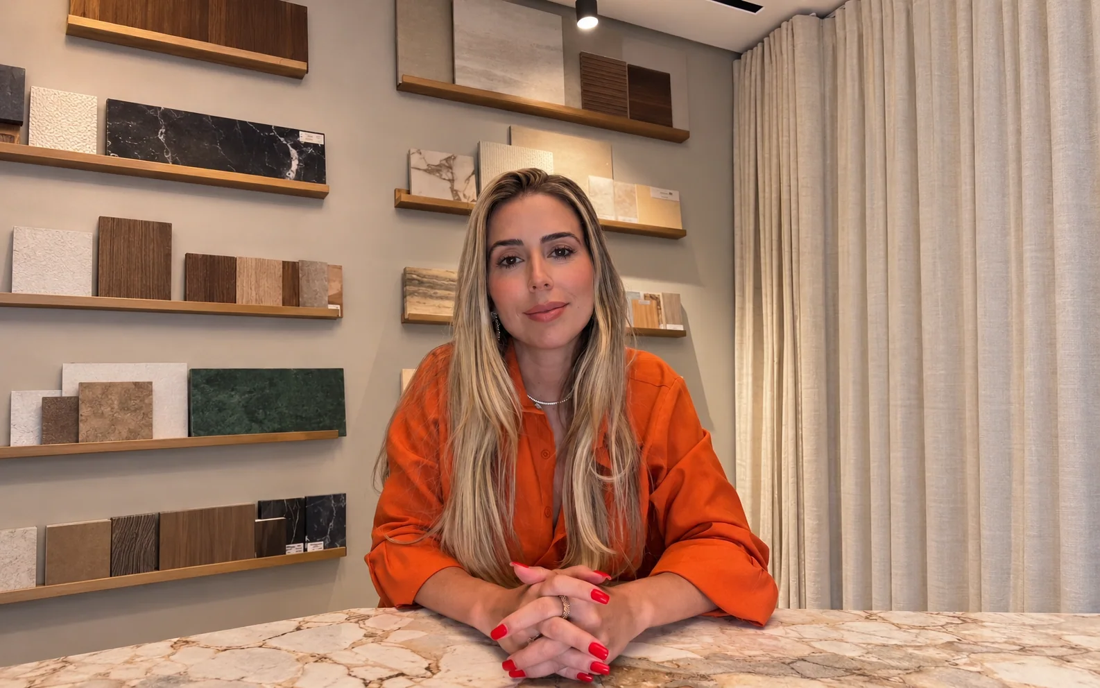Daniele Franco à mesa no showroom com amostras de revestimentos — capa adaptada da imagem original