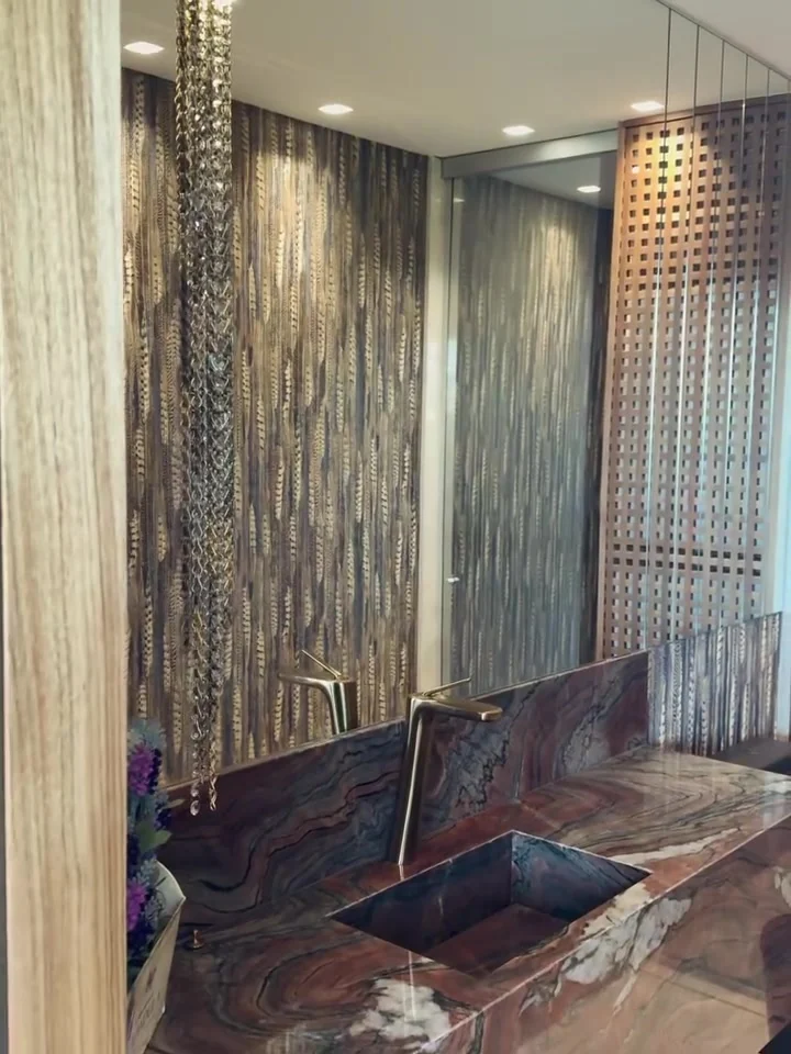 Lavabo com papel de parede de desenho vertical, bancada de veios marcantes, cuba retangular e metal em tom dourado