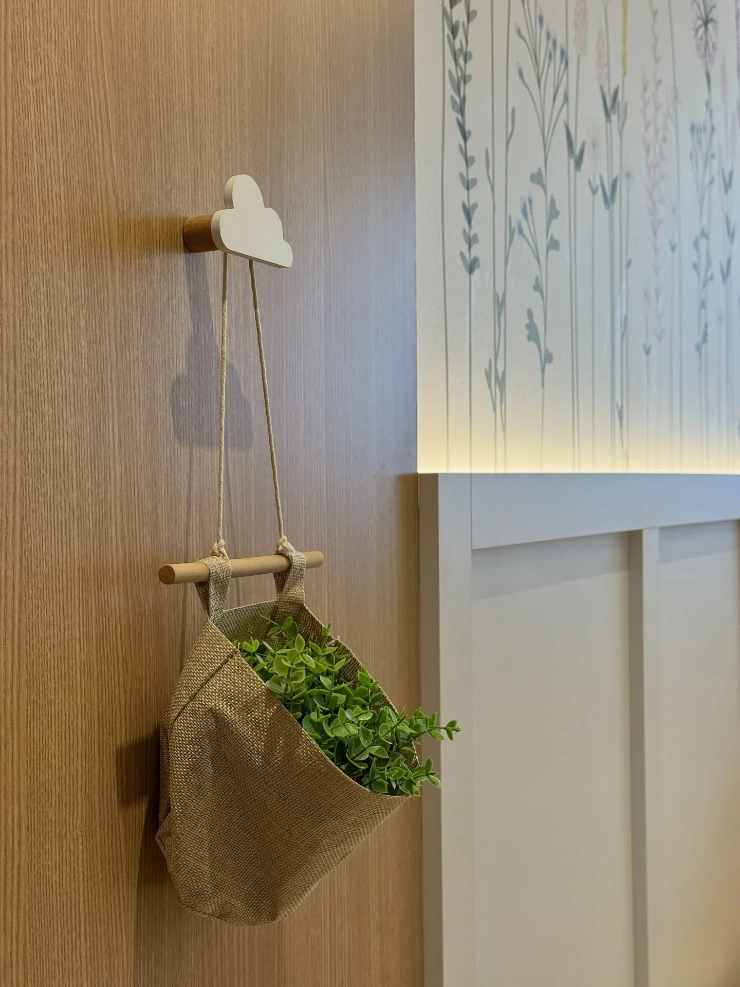 Detalhe de painel de madeira com pequeno cesto suspenso e parede floral ao lado