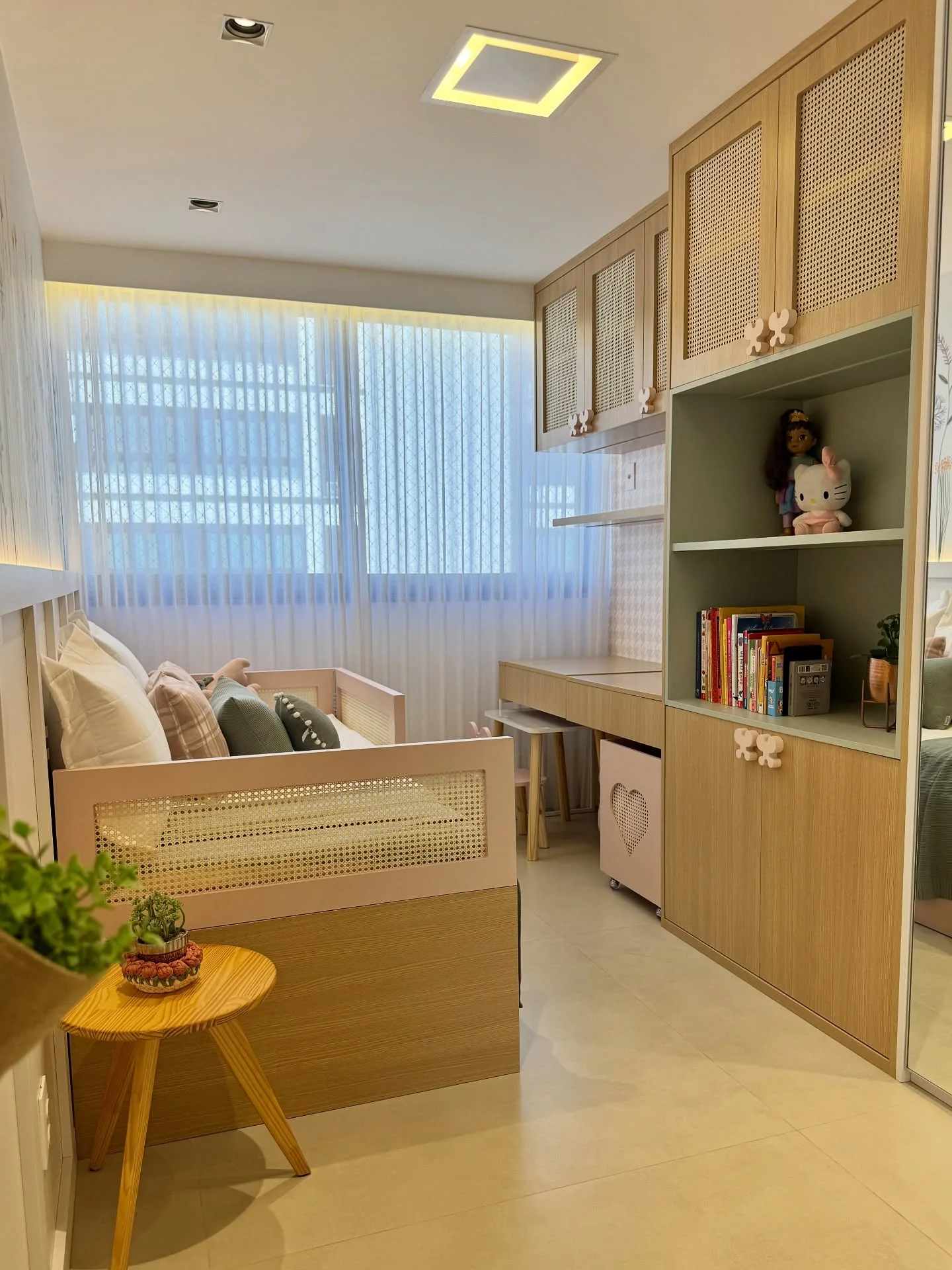 Visão ampla do quarto infantil com cama rosa e madeira, cortina clara e bancada de estudos