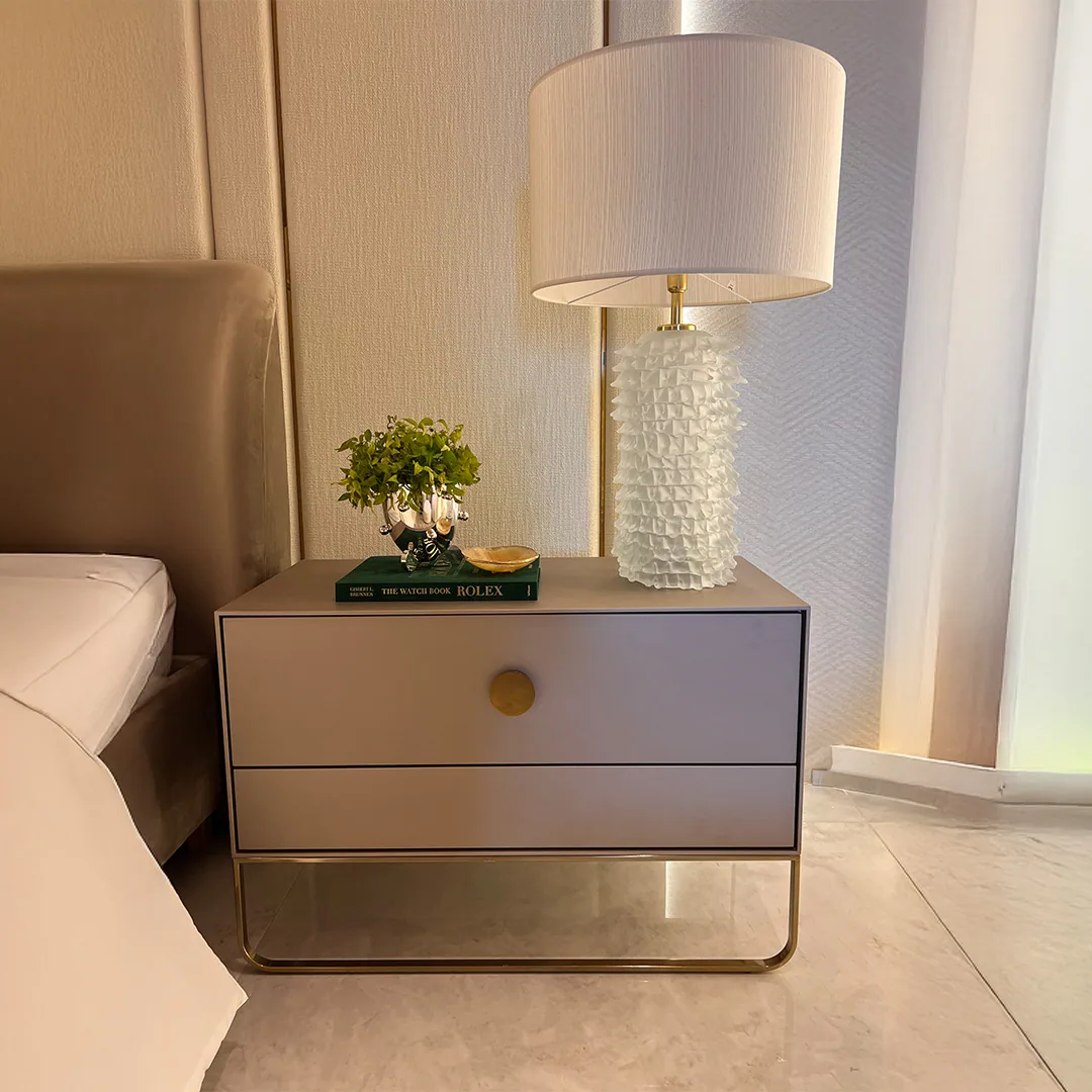 Detalhe de quarto com cabeceira estofada, mesa de cabeceira cinza, abajur branco texturizado e cortina clara