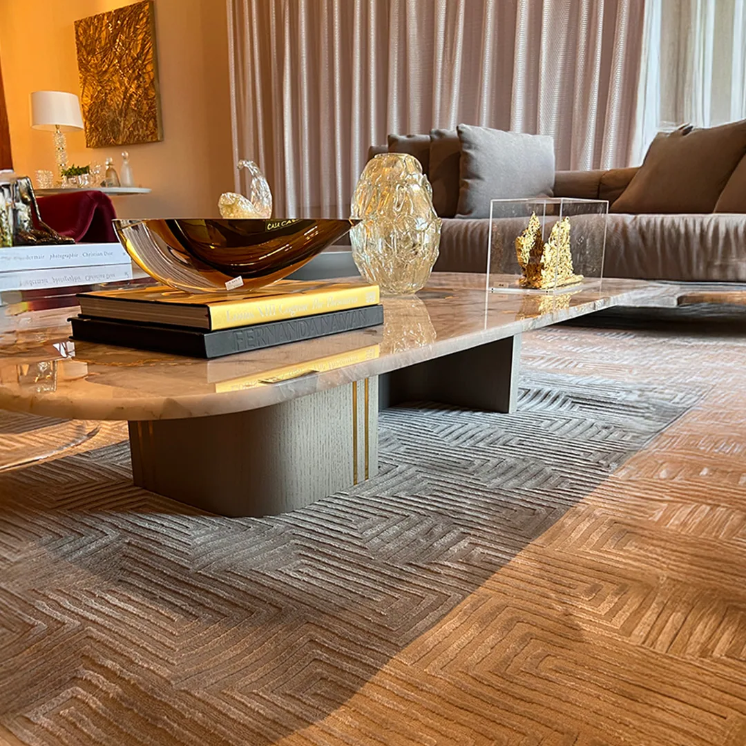 Mesa de centro de superfície com veios, objetos decorativos em tons âmbar e dourado, sofá e tapete com relevo geométrico