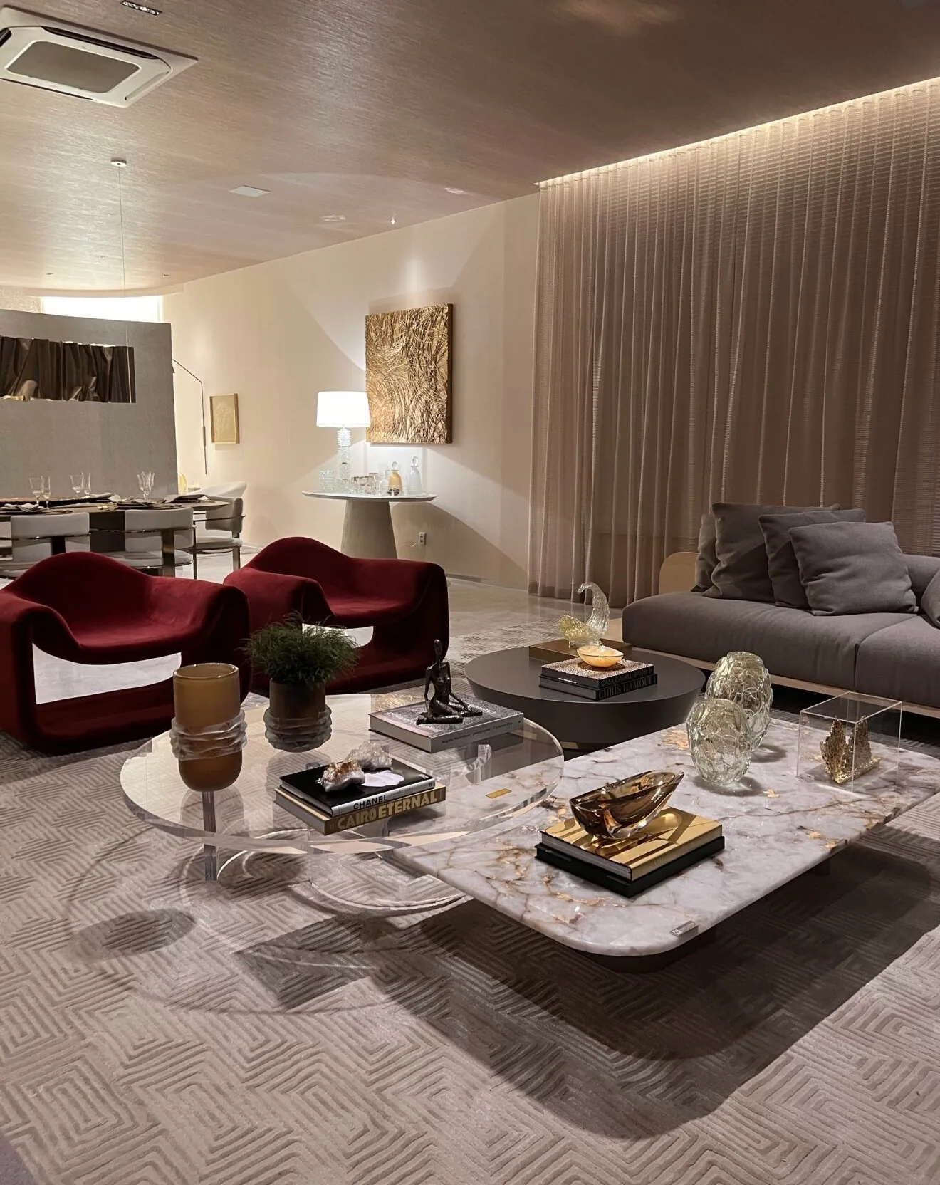 Sala com tapete claro, mesas de centro, poltronas e cortinas do piso ao teto