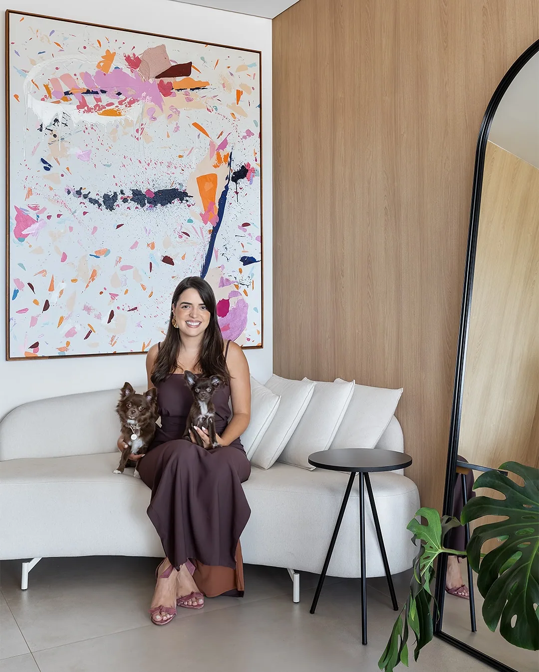 Milena Panhol sentada em uma sala junto a uma obra na parede